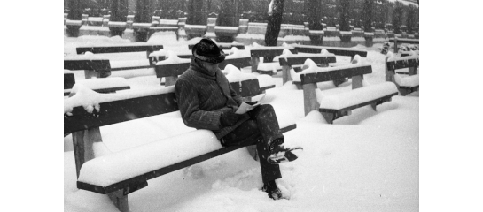 Man sitting and reading outside on a bench with snow all around