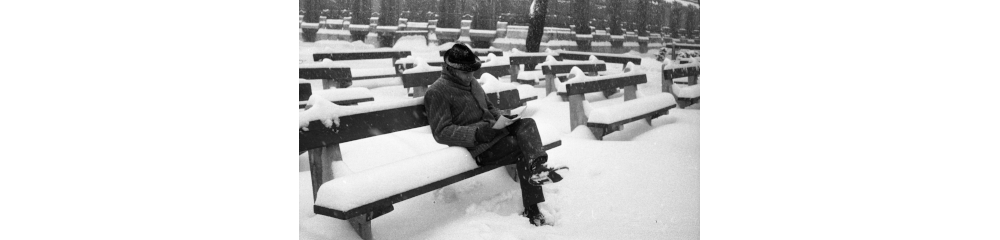 Man sitting and reading outside on a bench with snow all around